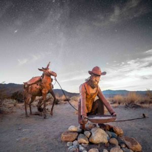 Metal gold miner and burro sculpture under a starry night sky in Borrego Springs, California.