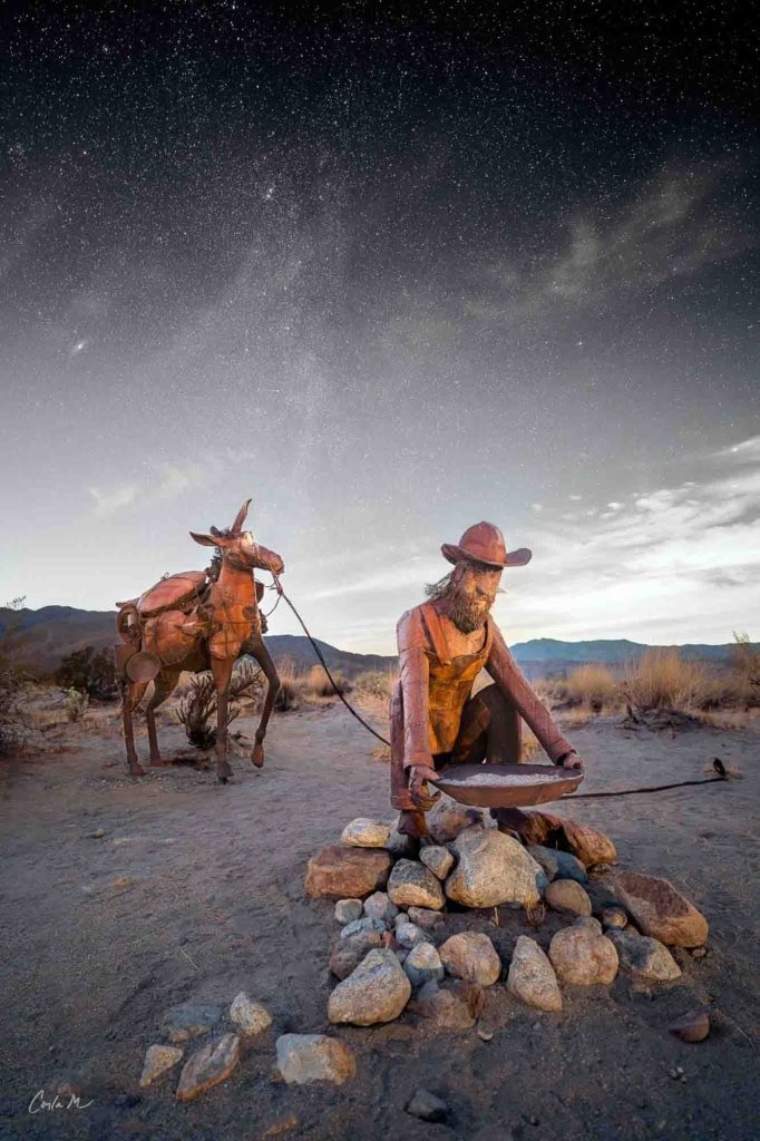 Metal gold miner and burro sculpture under a starry night sky in Borrego Springs, California.