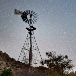 Historic windmill with stone water tank under a starry night sky at Chiricahua National Monument, Arizona.
