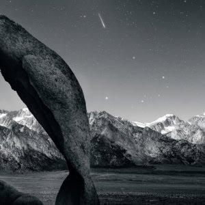 Cyclops Arch in Alabama Hills with a meteor and the Sierra Nevada mountain range in the background.