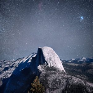 Moonlit Half Dome in Yosemite National Park with a starry sky and soft pine trees.