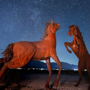A night photograph of two metal horse sculptures fighting under a starry sky in the Anza-Borrego Desert.