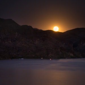 Full moon rising over Saguaro Lake in the Arizona desert with golden reflections on the water.