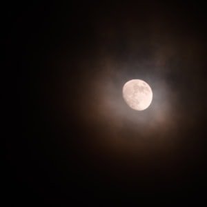 Abstract night photograph of a golden gibbous moon with clouds near Cyclops Arch in Alabama Hills, California.